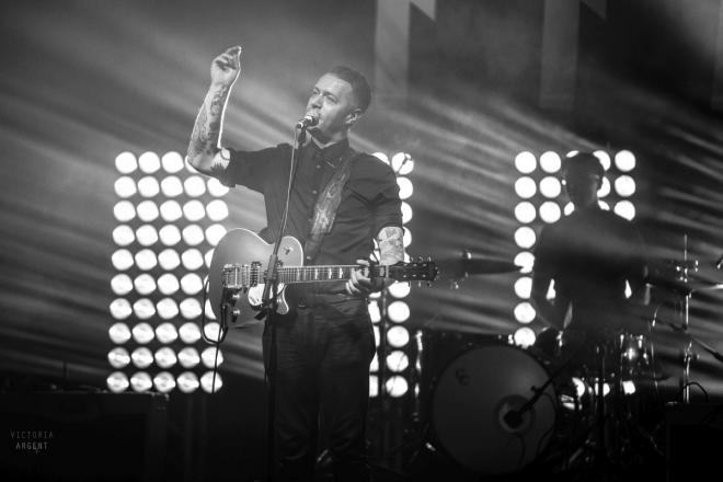 Zdjęcie z koncertu B90. Kind Dude. Gitarzysta przy mikrofonie z uniesioną ręką.