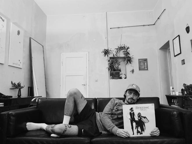 Mężczyzna leży na kanapie i trzyma płytę "Fleetwood Mac - "Rumors".