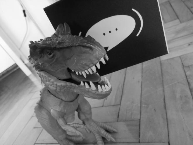 Zdjęcie plastikowego dinozaura trzymającego w paszczy album Łona i Webber - "Nawiasem mówiąc".
